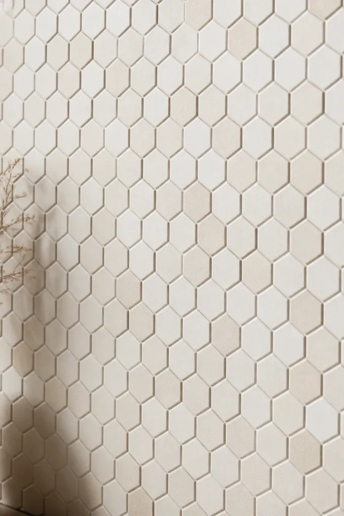 A honeycomb pattern of small raised hexagons across part of a wall; each hexagon is painted matte off-white with a slight beige tone variation. The pattern is tight with consistent spacing.