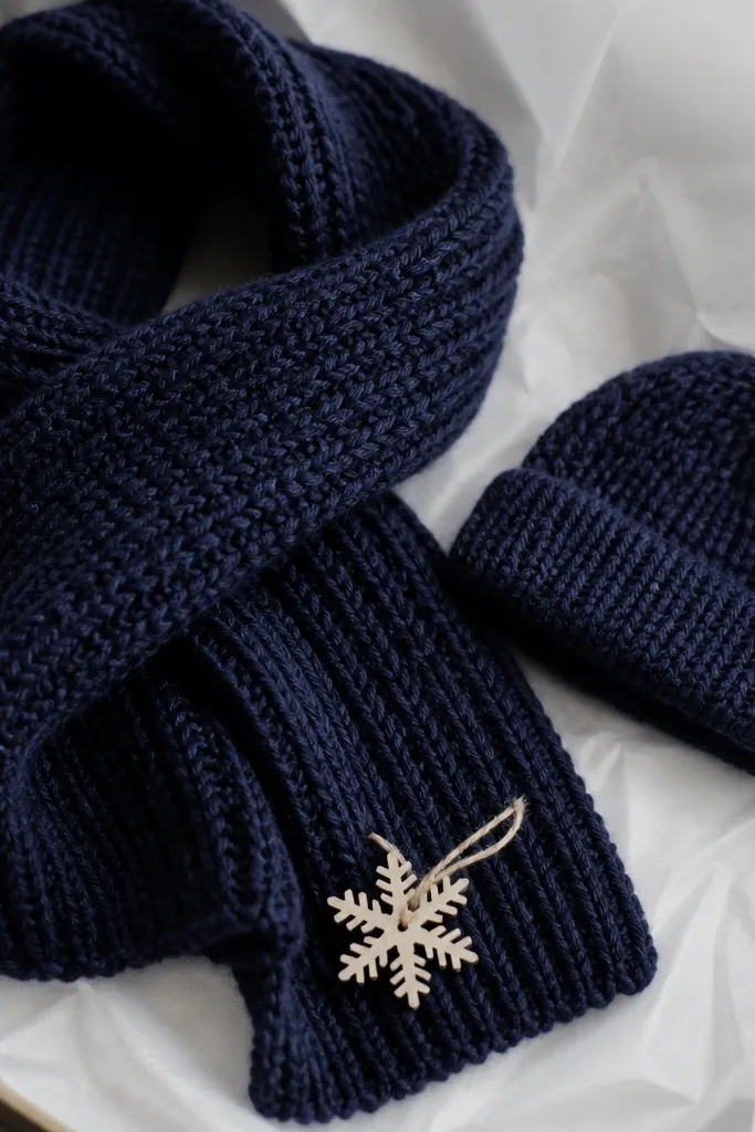 A dark navy scarf with a soft textured stitch and a matching mini beanie. Both sit on white tissue with a small snowflake tag tied to the scarf end.
