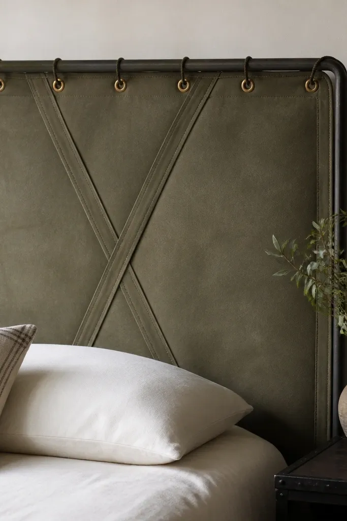 A headboard made from heavy outdoor canvas in a muted olive color. Two vertical canvas straps cross in the center, and brass eyelets show at the top where it's laced to a frame. The edges are wrapped and stitched.