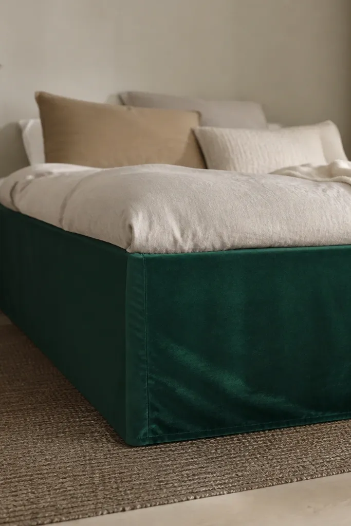 A Malm bed has a deep green velvet skirt panel that hangs straight and looks tailored. The fabric has a slight sheen and clean seams at the corners.