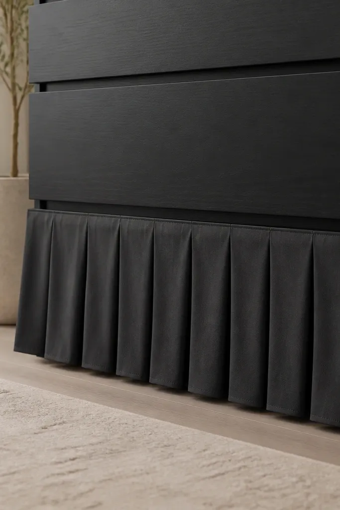 The bottom of a Malm dresser has a pleated fabric skirt in deep charcoal. The pleats are evenly spaced and the hem sits just above the floor.
