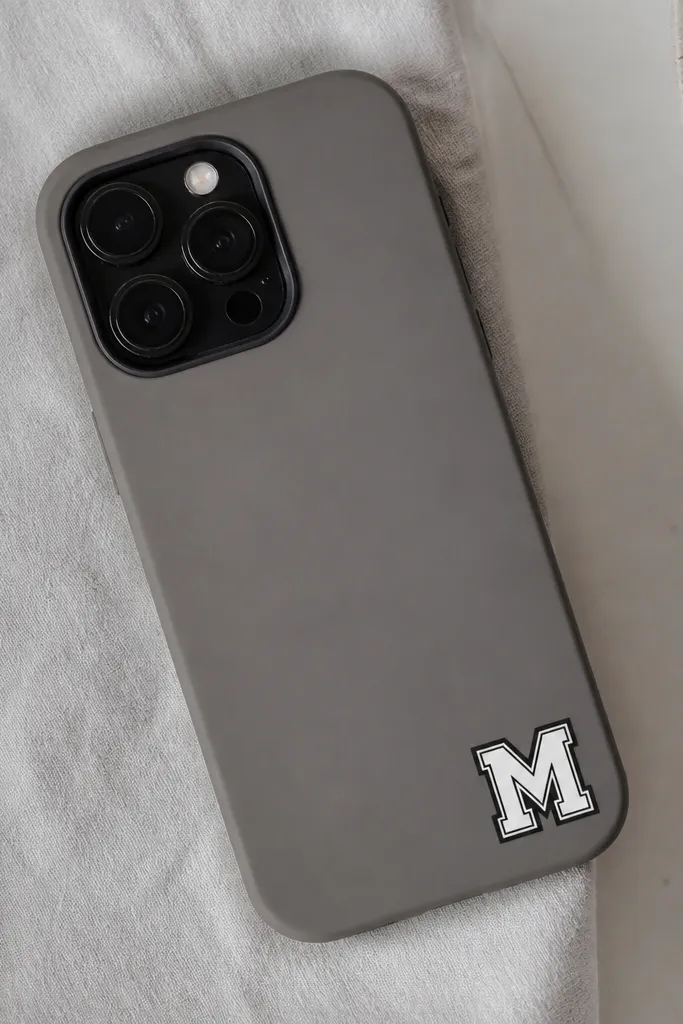 A matte gray phone cover with a white monogram letter in the bottom-right corner, surrounded by a thin black border like a cutout label.