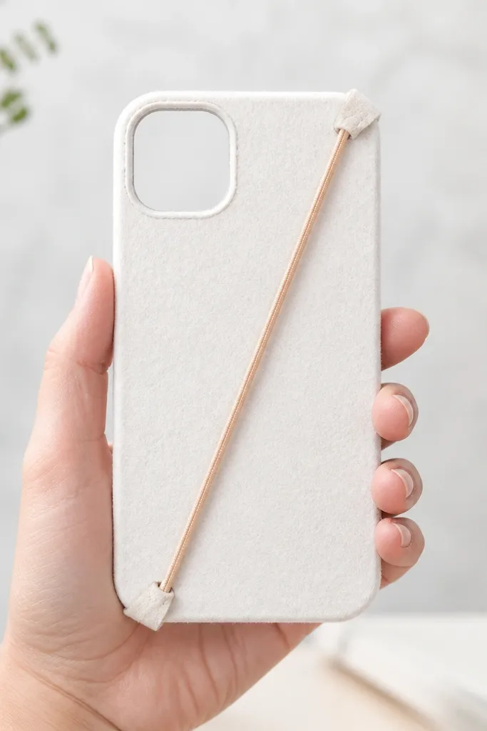A plain white felt phone back with two small corner loops made from elastic and a thin rubber band pulled through; it looks like a mini sports strap.