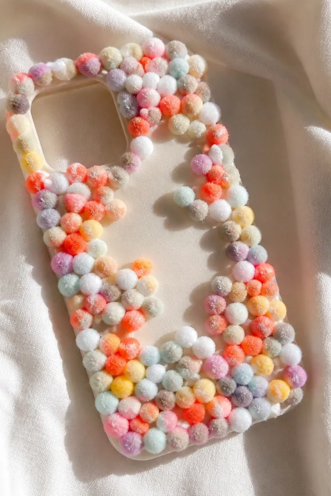 A phone cover covered in small pom-poms arranged like confetti. There's a smooth EVA backing that keeps the shape. The pom-poms are secured mostly around the edges and in clusters, with a clear camera cutout.